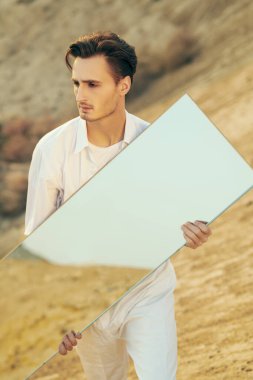 Moda fotoğrafı. Çölde ayna ile poz veren beyaz elbiseli romantik bir gencin portresi.. 