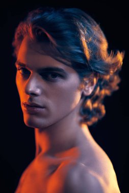 Güzel sarı saçlı, siyah arka planda karışık renkli ışık şeklinde poz veren yakışıklı bir atletik adamın yakın plan resmi. Erkek güzelliği. Spor ve sağlıklı yaşam tarzı.