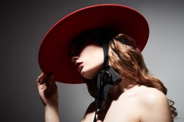 Siyah kravatlı, kırmızı şapkalı zarif üstsüz genç kadının portresi. Moda ve güzellik. Gri arkaplanda bir portre. 