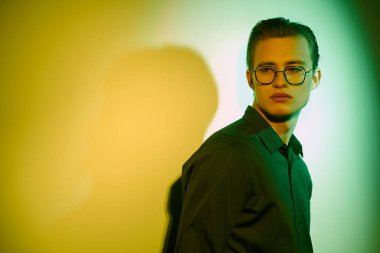 Yakışıklı genç adam duruyor, üzgün ve yalnız, duvara yaslanmış koyu yeşil ve sarı ışıklı.  