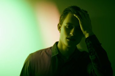 Yakışıklı genç adam, üzgün ve yalnız duruyor, koyu yeşil ışıkta duvara yaslanıyor. Duygular ve duygular. 