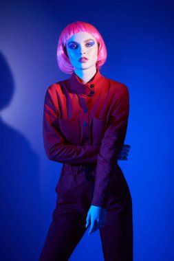 Parlak makyajlı, pembe saçlı, mavi arka planda poz veren muhteşem bir genç kadın portresi. Makyaj malzemeleri ve saç stili. Moda güzelliği trendleri.  