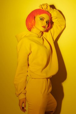 Parlak makyajlı ve kısa pembe peruklu çağdaş kız sarı ışıkta eşofman altında poz veriyor. Sportif şıklıkta. Gençlik modası ve güzellik eğilimleri. 