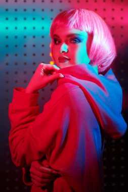 Parlak makyajlı, pembe saçlı, gece kulübünün neon pembe ve mavi ışıklarında poz veren modern bir kız. Disko tarzı. Gece partisi tarzı.. 