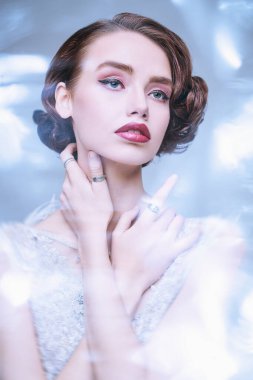 Açık mavi arka planda, lüks beyaz elbiseli çekici genç bir kadının portresi. Saçları ve makyajı 20 'li yılların tarzında. Akşam makyajı ve saç stili. 