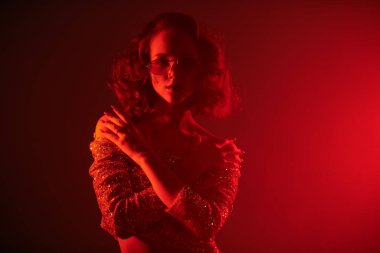 Parlak bluzlu ve şık güneş gözlüklü çekici kız dumandaki kırmızı ışıkta çekici. Gece partisi. Disko biçimi. 