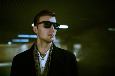 Şehir hayatı. Siyah ceketli ve siyah güneş gözlüklü bir adam yeraltı geçidinde duruyor ve uzaklığa bakıyor. Erkek stili. 