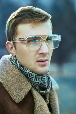 Gözlüklü zarif yakışıklı bir adamın dış mekâna bakan portresi. Erkek modası.