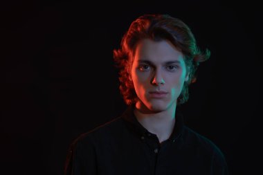 Koyu arkaplanda dalgalı sarı saçlı, parlak ve gölgeli yakışıklı bir gencin portresi. Erkeklerin güzelliği. 