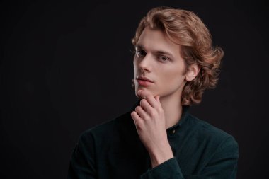 Siyah arka planda dalgalı sarı saçlı yakışıklı bir gencin portresi. Erkeklerin güzelliği. 