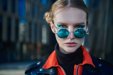 Parlak makyajlı, şık renkli elbiseli, büyük bir caddede poz veren modaya uygun bir model. Modern gençlik giyim eğilimleri. 