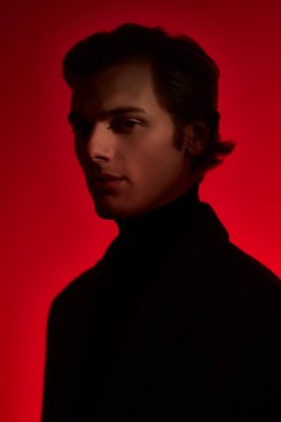 Zarif elbiseli yakışıklı genç adam kırmızı arka planda kırmızı ışıkta stüdyoda poz veriyor. Sanat portresi. Erkek stili. 