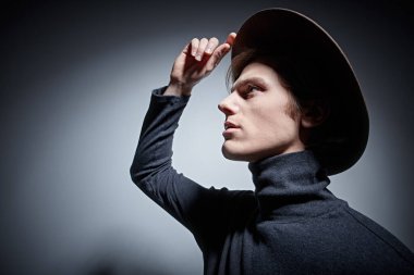 Geniş kenarlı şapkalı ve balıkçı yaka kazaklı yakışıklı bir genç. Kopyalama alanı olan gri bir arkaplan. Erkek stili. 