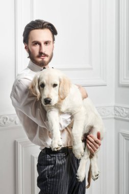 Klasik takım elbiseli yakışıklı genç adam Golden Retriever köpeğini tutuyor. 