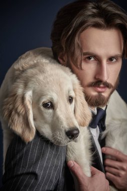 Zarif takım elbiseli yakışıklı bir adamın portresi Golden Retriever köpeğini tutuyor. Erkek modası.