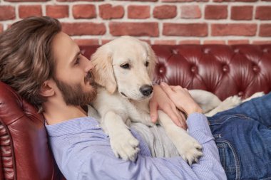 Mutlu genç adam evcil köpeği Golden Retriever ile kanepede yatıyor..