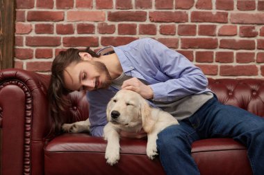 Evcil köpeği Golden Retriever ile evdeki kanepede oturan yakışıklı genç adam..