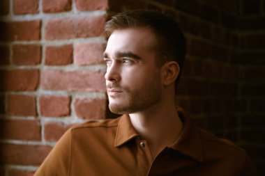 Duvarın arkasındaki pencereden dışarı bakan yakışıklı, olgun bir adamın portresi. Erkek güzelliği, moda.