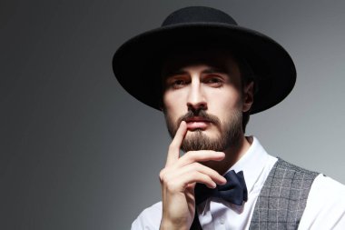 Zarif klasik takım elbiseli yakışıklı bir esmer adam portresi ve gri arka planda siyah bir şapka. Erkek güzelliği. Moda..