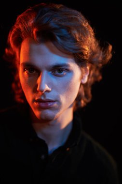 Siyah arka planda dalgalı saçlı, karışık renkli ışık saçan yakışıklı bir gencin portresi. Erkek güzelliği. Boşluğu kopyala.