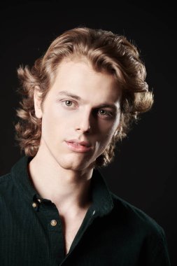 Dalgalı sarı saçlı yakışıklı genç adam kameraya bakarak gülümsüyor. Kopyalama alanı olan siyah arkaplan. Erkeklerin güzelliği.