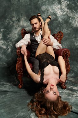 İç çamaşırlı seksi kız, grunge apartmanında eski bir koltukta oturan bir adamın üzerinde yatıyor. Aşk oyunları. Göz kamaştırıcı yaşam tarzı.