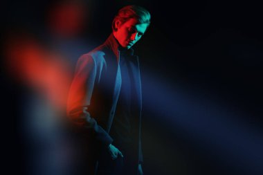 Stüdyoda renkli ışıkta şık kıyafetler içinde poz veren zarif bir gencin portresi. Moda fotoğrafı..