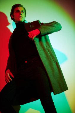 Stüdyoda renkli ışıkta şık kıyafetler içinde poz veren zarif bir gencin portresi. Moda fotoğrafı..