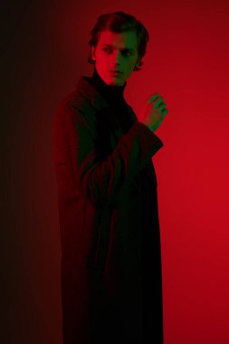 Stüdyoda karanlıkta kırmızı ışıkta poz veren zarif elbiseli yakışıklı bir gencin portresi. Erkek stili.