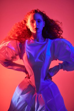 Beyaz bir sanat elbisesi içinde poz veren gür kırmızı kıvırcık saçlı sofistike bir kadın modelin portresi. Karanlık bir odada koyu kırmızı ışıklı bir stüdyo portresi. Moda sanatı. 