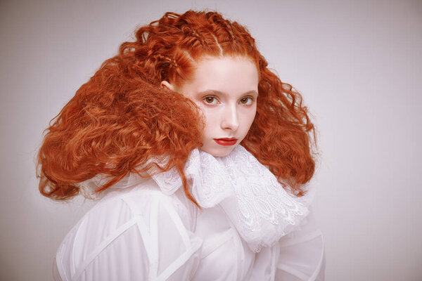 Close up portrait of a refined fashion model girl with lush red curly hair posing in a white haute couture dress. Studio shot on light grey background. 