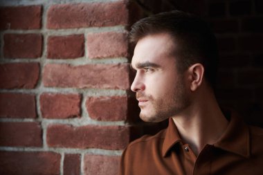 Duvarın arkasındaki pencereden dışarı bakan yakışıklı olgun bir adamın portresini yakından çek. Erkek güzelliği, moda.