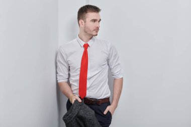 Beyaz gömlekli ve kırmızı kravatlı yakışıklı adam beyaz duvarın yanında poz veriyor. İş adamı portresi. 