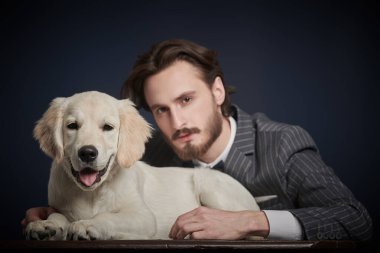 Zarif takım elbiseli yakışıklı beyefendi koyu mavi arka planda Golden Retriever köpeğiyle poz veriyor. Moda, insan ve köpek. 