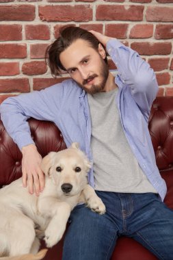 Evcil köpeği Golden Retriever ile evdeki kanepede oturan mutlu genç adam..
