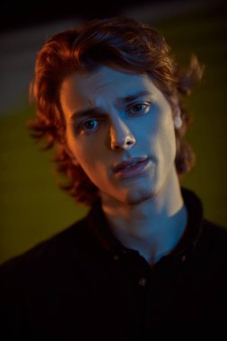 Koyu arkaplanda dalgalı kızıl saçlı, parlak ve gölgeli yakışıklı bir genç. Erkeklerin güzelliği. 