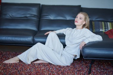 Güzel, mutlu bir kız oturma odasında dinleniyor. Kanepenin yanındaki yumuşak halıda oturuyor. Yaşam tarzı. Evin içi, mobilyalar.. 