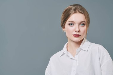 Sarışın ve doğal makyajlı güzel bir genç kadının portresi. Fotokopi alanı olan gri bir arkaplanda stüdyo çekimi. Güzellik endüstrisi.