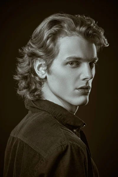 Black-and-white portrait of a handsome young man with wavy blond hair looking up on a black background. Side view. Men\'s beauty.