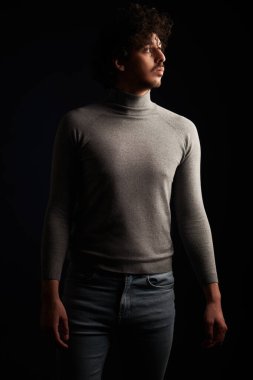 Kıvırcık siyah saçlı yakışıklı bir gencin portresi siyah arka planda, karanlıkta başka yöne bakıyor. Erkeklerin güzelliği.