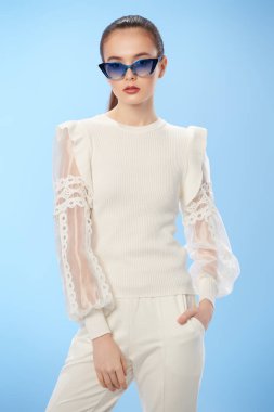 Zarif beyaz elbiseler ve açık mavi arka planda güneş gözlüğü takan güzel bir yaz kızı. Mutlu gülümseyen kız. Yaz modası ve makyaj.