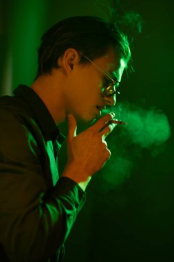 Genç adam koyu yeşil ışıkta sigara içiyor. Kötü alışkanlıklar. Sigara molası..