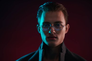 Yakışıklı, şık bir genç adamın portresi. Palto ve şık gözlüklerle poz veriyor. Erkek modası. Erkekler için optik.