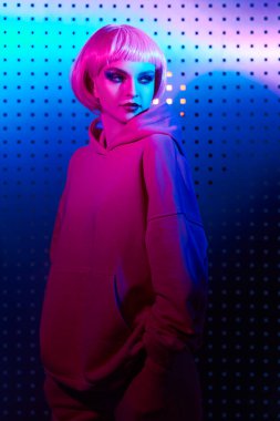 Parlak makyajlı, pembe saçlı, gece kulübünün neon pembe ve mavi ışıklarında poz veren modern bir kız portresi. Disko tarzı. Gece partisi tarzı.. 