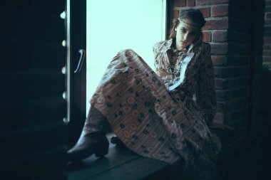 Saç stili ve makyajlı güzel bir kız evdeki pencere eşiğinde dalgın bir şekilde oturuyor..