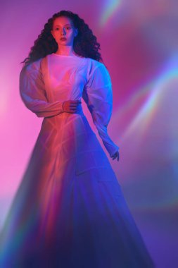 İnce, kırmızı kıvırcık saçlı, uzun beyaz fütüristik elbisesi ve neon kırmızısı ışıklandırmasıyla poz veren zarif bir kadın modelinin sanat portresi..