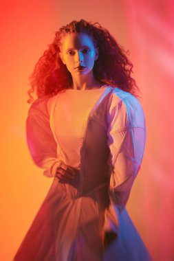 Uzun beyaz bir fütüristik elbiseyle karışık kırmızı ışıkların arasında poz veren, gür kırmızı kıvırcık saçlı, zarif bir kadın modelinin sanat portresi..