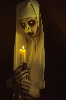 Korkunç şeytan ruhlu bir rahibe elinde mumla karanlık bir odada duruyor. Korku ve Cadılar Bayramı.