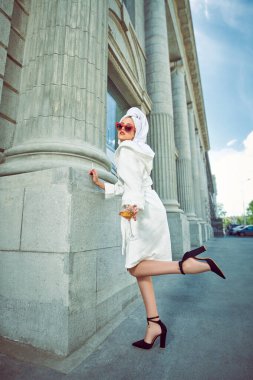 Kafasında beyaz bir havluyla beyaz sabahlık giymiş, bir bardak şarap ve sigarayla şehir caddesinde çekici bir kadın. Moda fotoğrafı. Göz kamaştırıcı yaşam tarzı. 