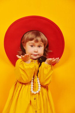 Şirin küçük kız modası. Kırmızı şapkalı ve sarı elbiseli sevimli küçük kız kameraya baktı ve şaşırdı. Mutlu çocukluk.